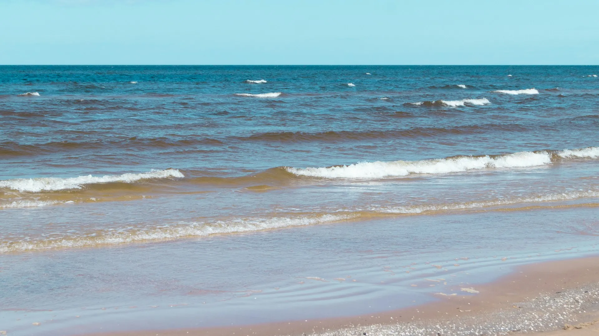Wide white-sand beach at Jūrmala with gentle Baltic waves and scattered beachgoers on a summer day