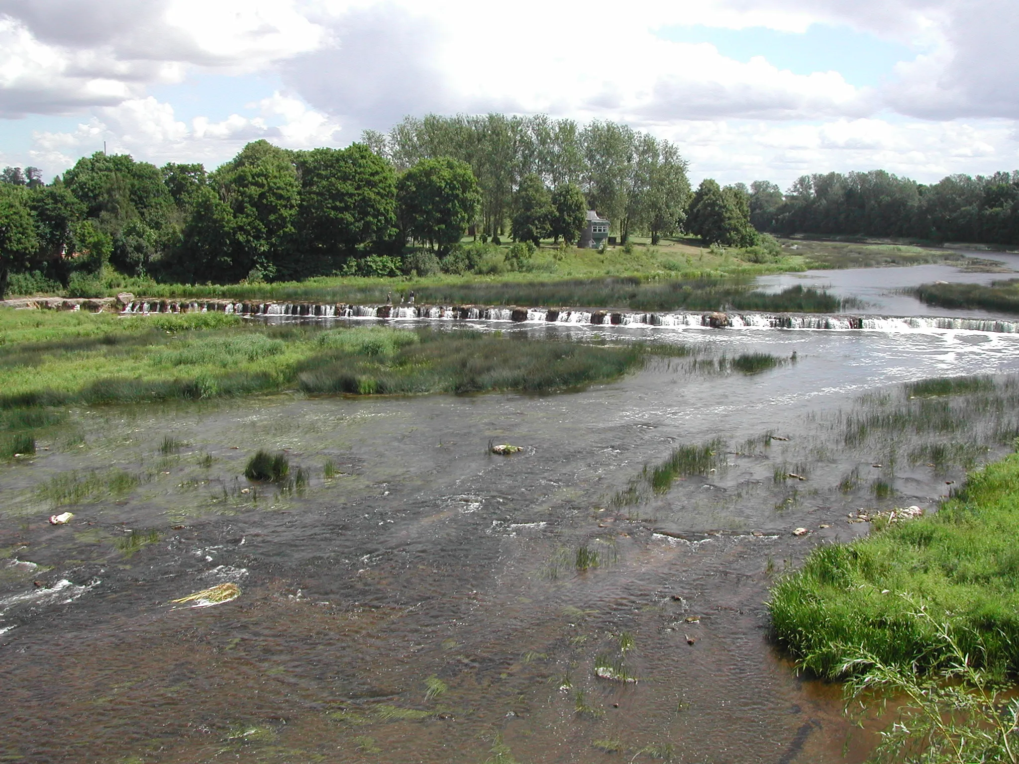 The Venta Rapid in Kuldīga, a broad low waterfall across the river with a historic brick bridge in the background