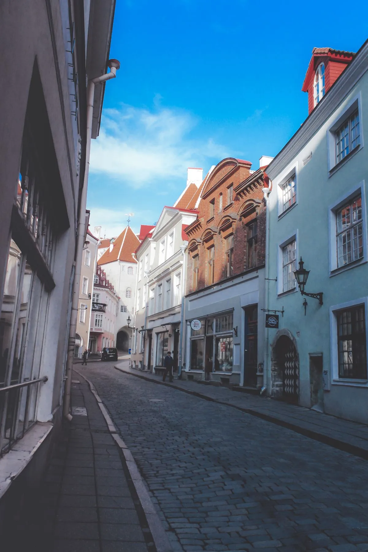 A cobblestone street in Tallinn Old Town lined with pastel-coloured medieval buildings under a spring sun